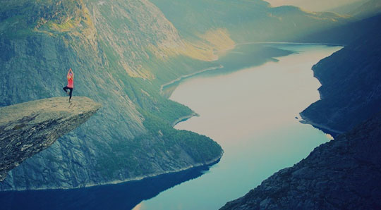 Woman doing yoga on top of a mountain overlooking a river