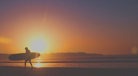 Surfer walking on the beach at sunset